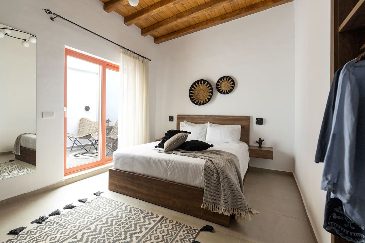 Un dormitorio con cama de madera, alfombra estampada y vistas al exterior.