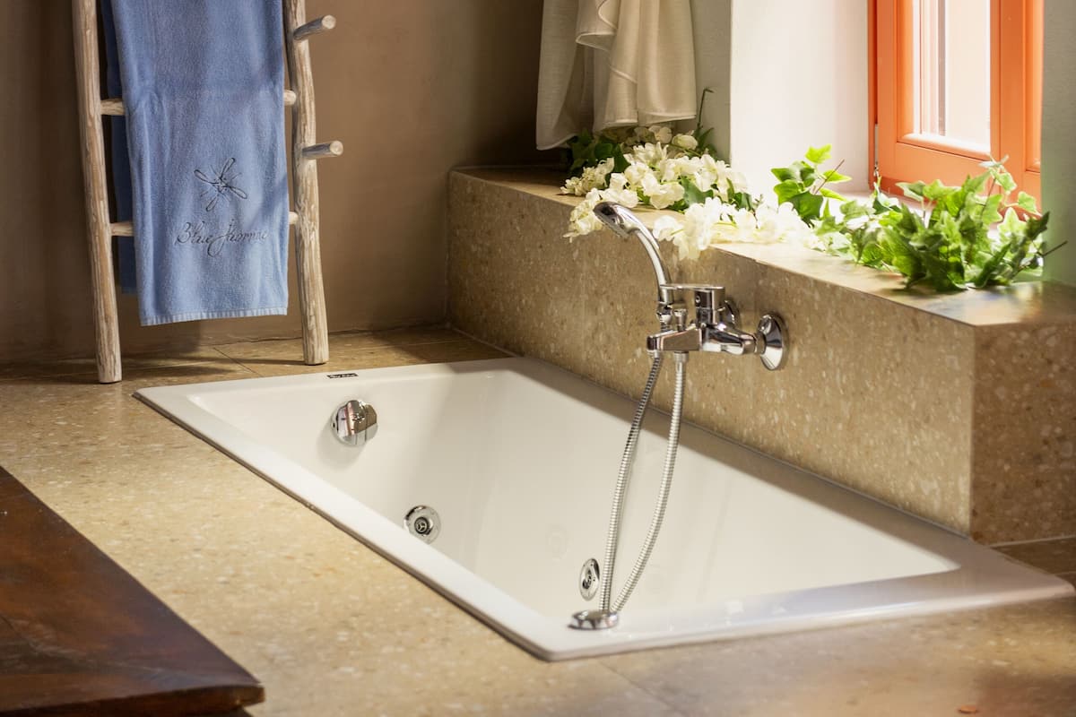 Un baño con una bañera, una escalera de madera, un perchero para toallas, un ventanal con marco naranja y una pequeña maceta con flores.