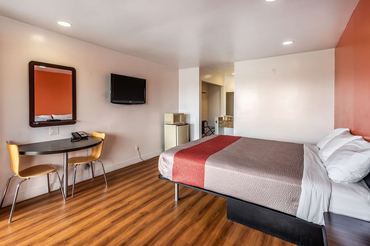 A hotel room with a bed, a desk with two chairs, a television mounted on the wall, and a microwave.