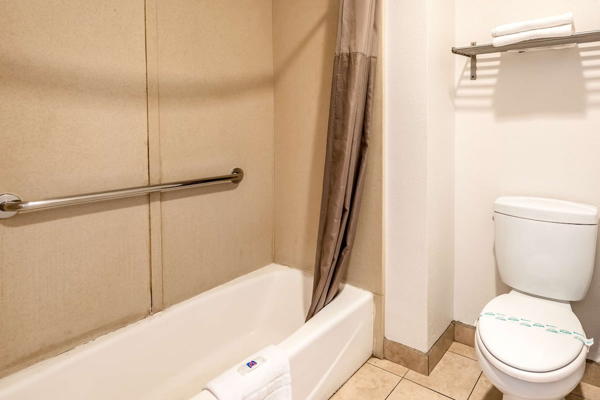 A bathroom with a bathtub, a shower curtain, a toilet, and a towel rack.