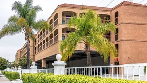 A multi-story building with a red-tiled roof, a white fence, and palm trees. - Motel 6 Gardena, CA - South (Gardena)