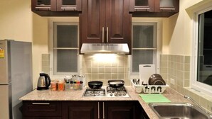 A kitchen with dark wooden cabinets, a stainless steel range hood, a gas stove, and a sink. - Cozy House Huahin (Hua Hin)