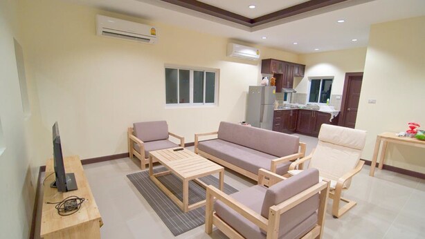 A modern living room with a sofa, chairs, a coffee table, and a TV on a wooden stand. - Cozy House Huahin (Hua Hin)