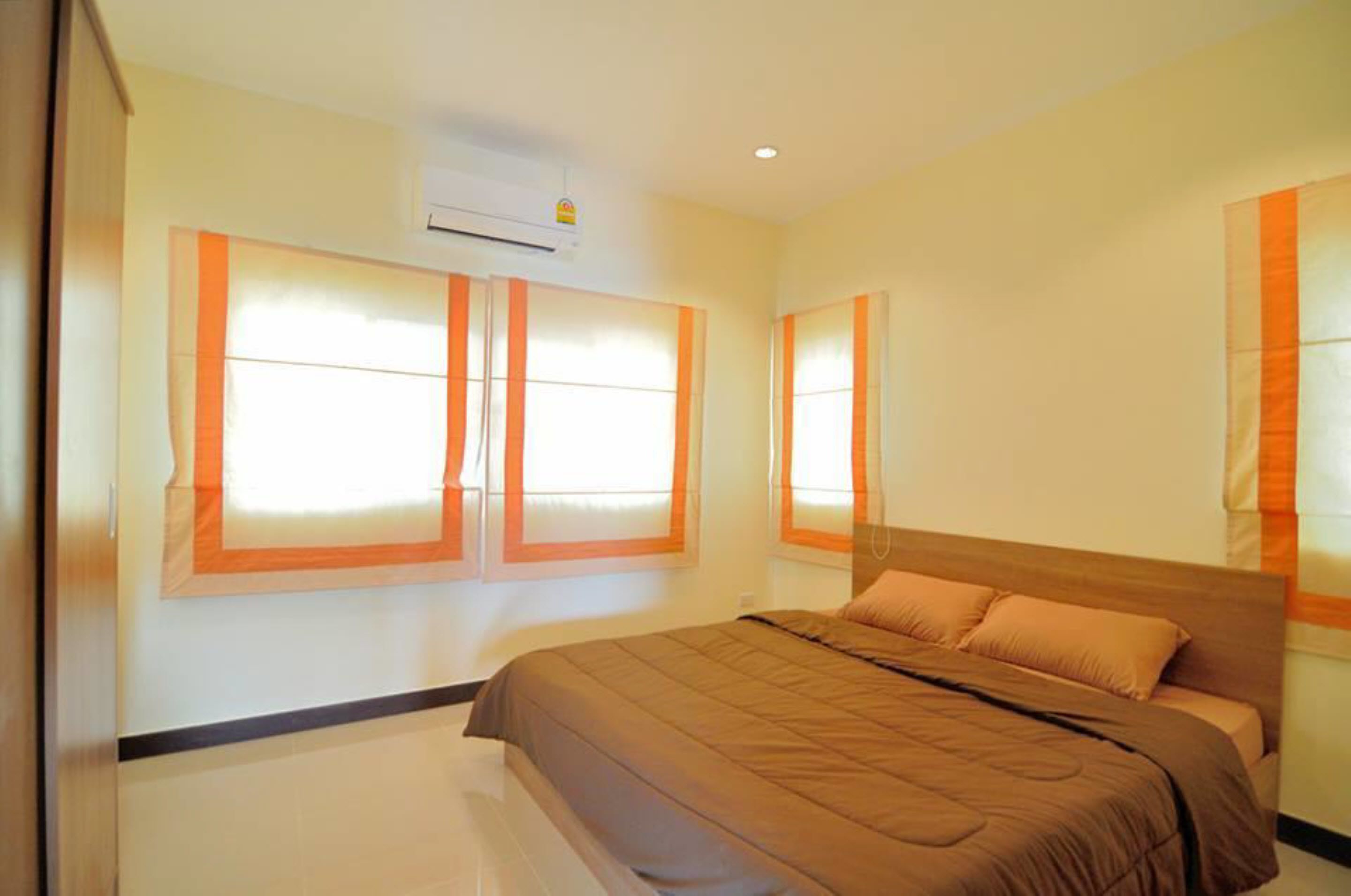 Un dormitorio con una cama grande, dos ventanas con persianas naranjas y un equipo de aire acondicionado en la pared.