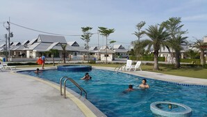 A swimming pool area with multiple pools, lounge chairs, and palm trees. - Cozy House Huahin (Hua Hin)