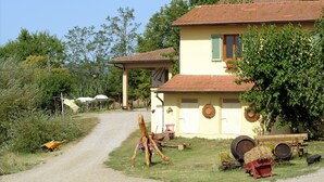 A rustic house with a dirt path leading to it, surrounded by greenery and farm equipment. - Agriturismo Podere Poggio Ai Cieli (San Gimignano)