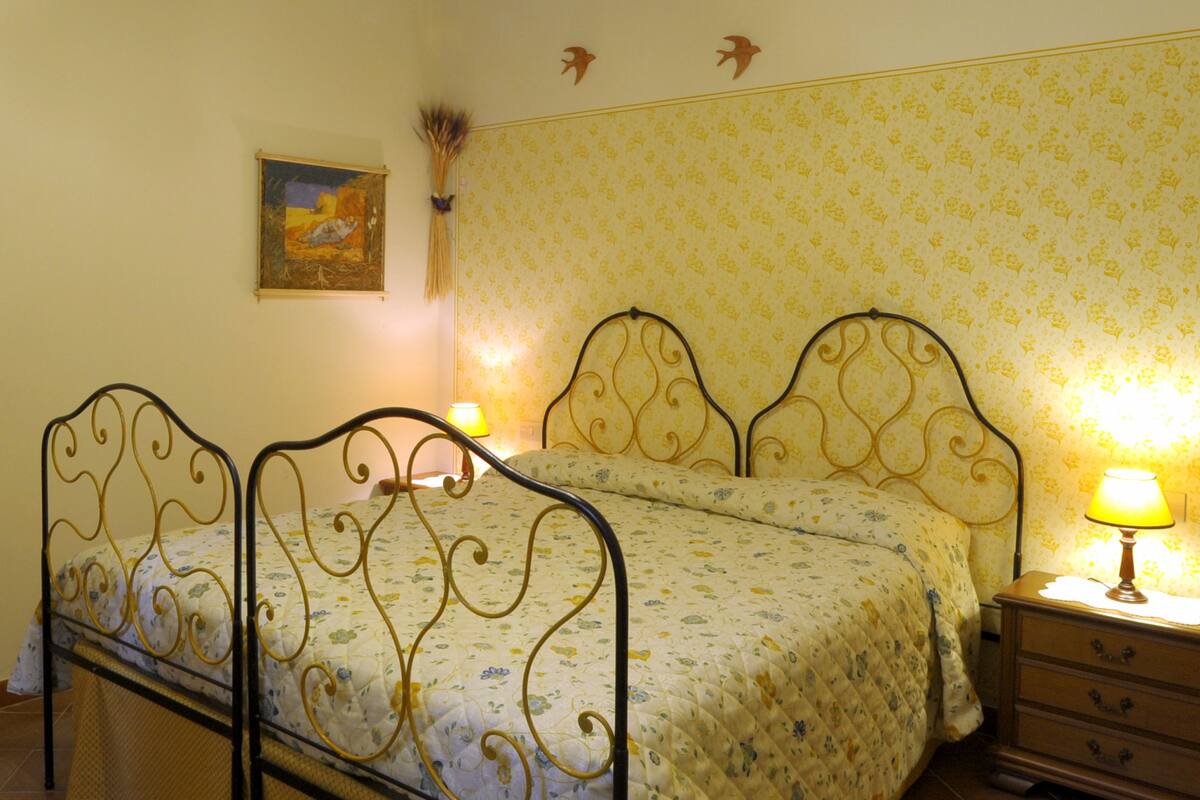 A bedroom with a double bed, a nightstand, a lamp, a wall clock, and a painting.