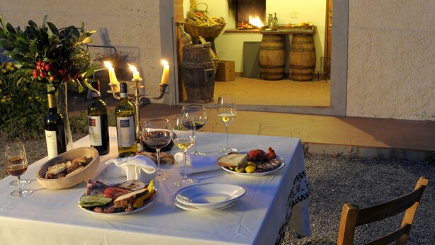 An outdoor dining table set with wine glasses, plates of food, and candles. - Agriturismo Podere Poggio Ai Cieli (San Gimignano)