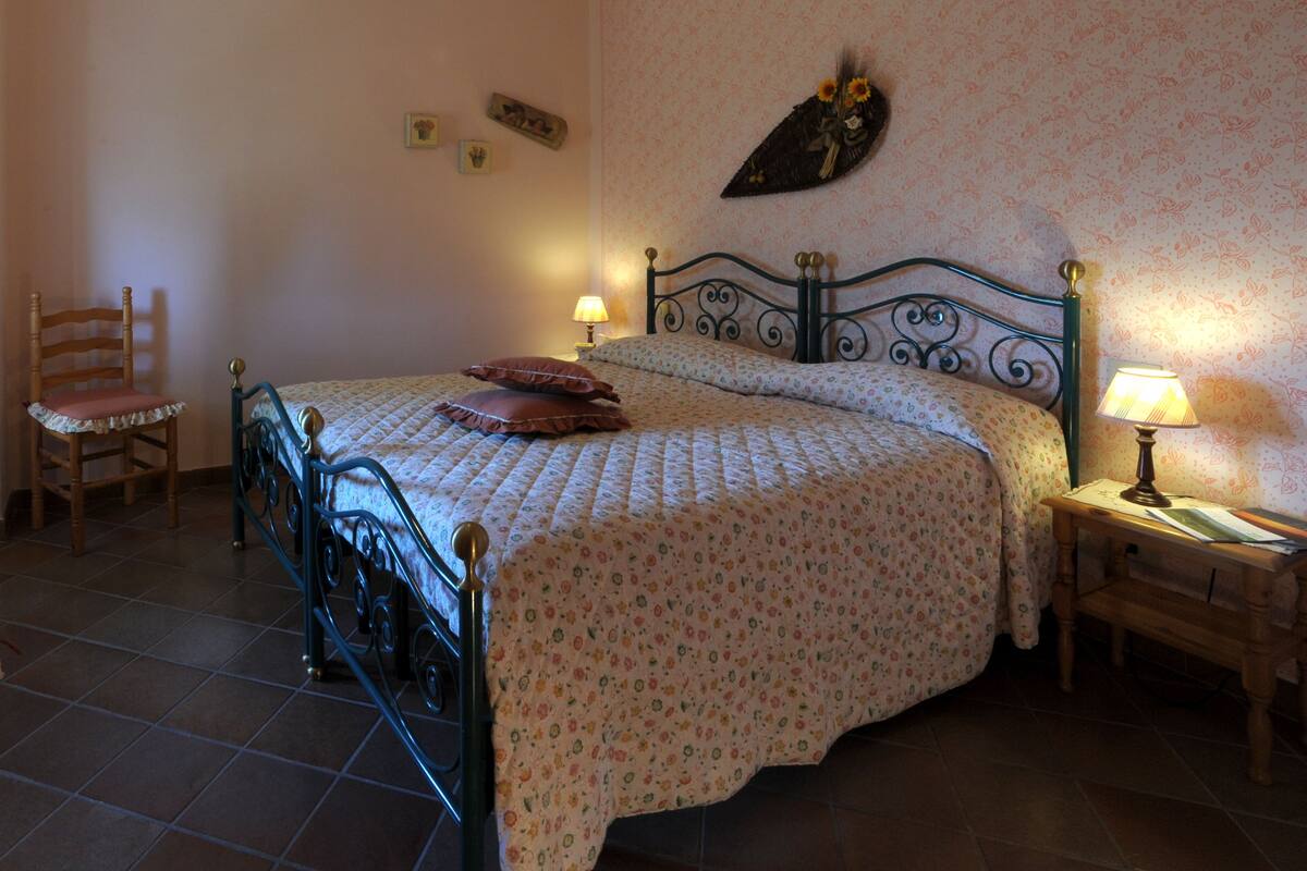 A bedroom with a bed, a chair, a nightstand with a lamp, and a wall-mounted decoration.