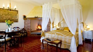 A four-poster bed with a canopy, a fireplace, a chessboard, and a dining area with chairs and a table. - Agriturismo Podere Poggio Ai Cieli (San Gimignano)