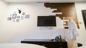 Un dormitorio con cama, cómoda, televisor montado en la pared y cabecero de madera.