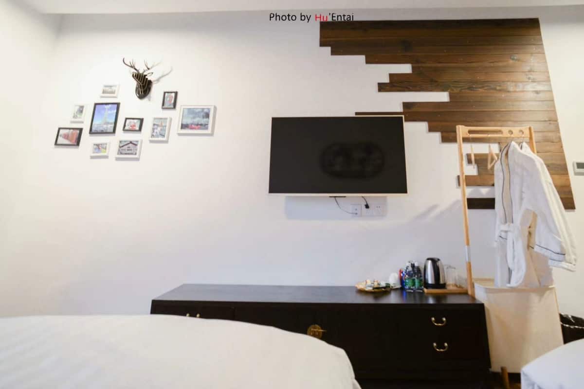 A bedroom with a bed, a dresser, a TV mounted on the wall, and a wooden headboard.