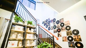 Una escalera con barandilla metálica, rodeada de estantes con plantas en macetas y bolsas, y una pared decorada con discos de vinilo y carteles.