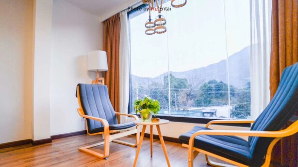 Una habitación con dos sillas azules, una pequeña mesa de madera con una planta y un ventanal con vistas a montañas.