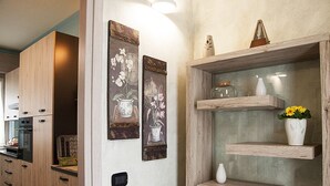 Cozinha com armários de madeira, forno embutido e prateleira na parede com objetos decorativos.