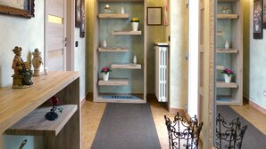 Um corredor com prateleiras de madeira exibindo vasos e flores, um radiador e um tapete com a palavra 'HOME'.