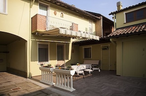 Un edificio de dos pisos con un balcón, un patio con mesa y sillas, y un garaje.