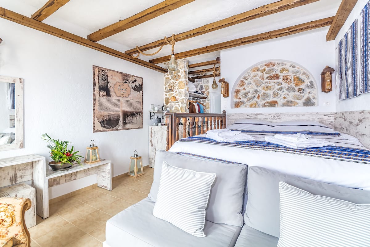 Ein Schlafzimmer mit Steinwand, Bett mit weißer und blauer Bettwäsche, Holz-Kopfende und Kamin aus Stein.