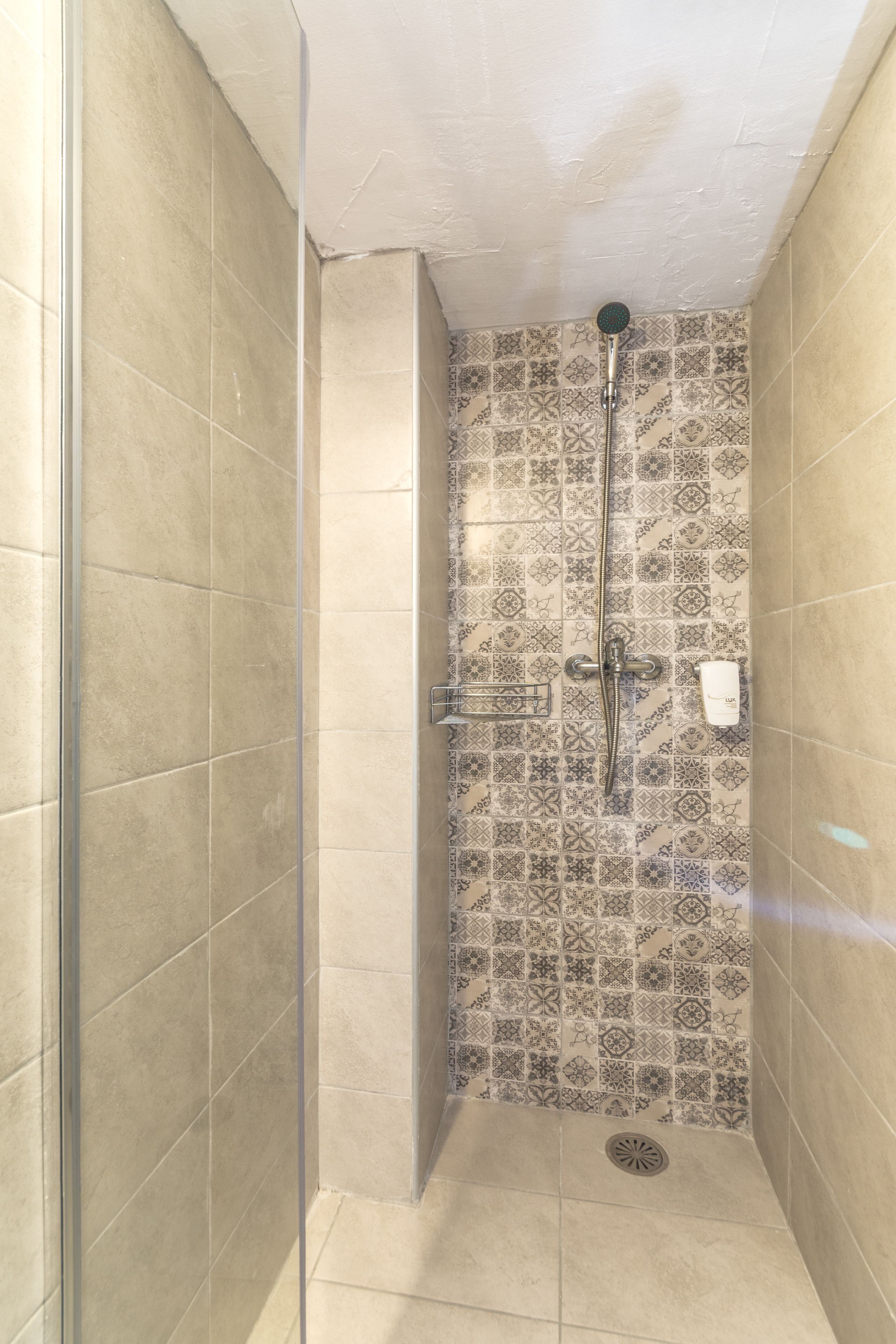 Eine Dusche mit Glastür, gefliesten Wänden mit Muster und einer Duschbrause.