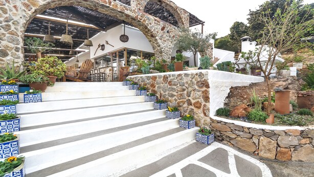 A stone staircase leading to a building with a rustic interior, surrounded by potted plants and outdoor seating. - Limeri Traditional Guest House (Rhodes)