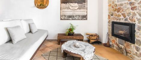 A living room with a sofa, a small wooden table with a plant, a decorative wall piece, and a fireplace.