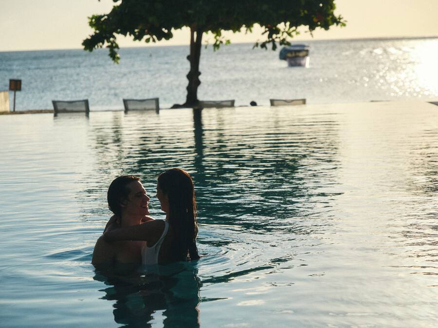 Una persona en una piscina con vista al mar y un árbol al fondo.