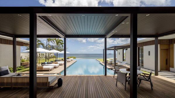 A modern poolside area with lounge chairs, a wooden deck, and a view of the ocean. - Silversands Grand Anse (St. George's)
