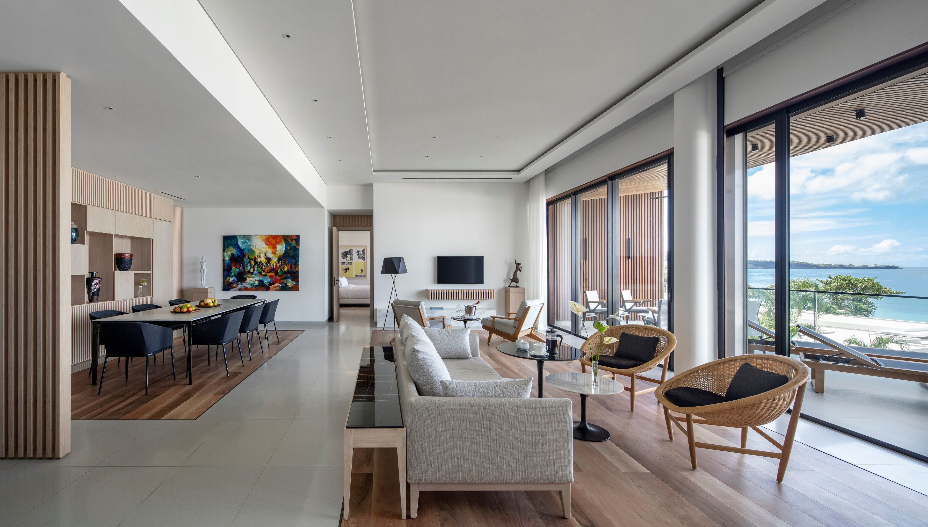 Una sala de estar moderna con comedor, ventanas amplias con vista al mar y un televisor de pantalla plana montado en la pared.