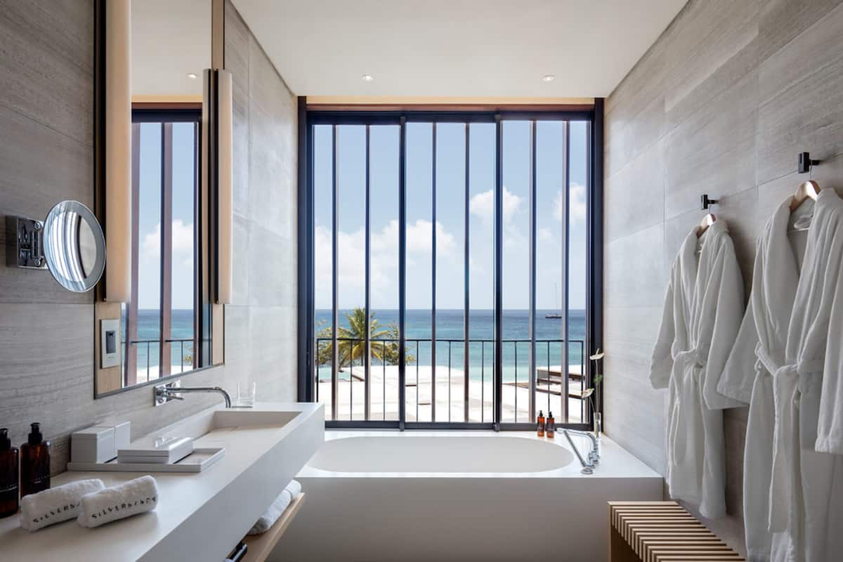 A modern bathroom with a large window, a bathtub, and a vanity with toiletries.