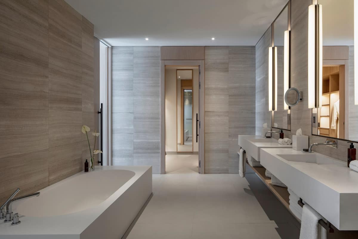 A modern bathroom with a large bathtub, two sinks, and a walk-in shower.