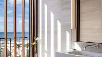 A modern bathroom with a large bathtub, a vanity with a mirror, and a view of the ocean.