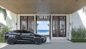 A modern building with a black car parked in front, large windows, and a view of the ocean. - Silversands Grand Anse (St. George's)