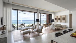 A spacious living area with a large window overlooking the sea, furnished with a sofa, chairs, and a dining table. - Silversands Grand Anse (St. George's)