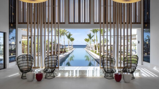 A modern hotel lobby with a pool view, wooden slats, and black wireframe chairs. - Silversands Grand Anse (St. George's)