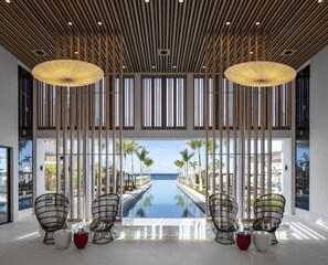 A modern hotel lobby with a pool view, wooden slats, and black wireframe chairs. - Silversands Grand Anse (St. George's)