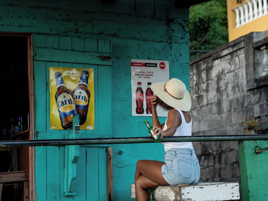 Una persona sentada en un banco frente a un edificio con un cartel de botellas de cerveza en la pared.