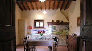 A rustic kitchen with a tiled backsplash, wooden cabinets, and a dining table with chairs. - Tenuta Monti (Borgo San Lorenzo)