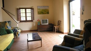 A cozy living room with a sofa, armchair, and a small table. There's a window with shutters, a painting on the wall, and a television on a wooden cabinet. - Tenuta Monti (Borgo San Lorenzo)