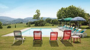 A pool area with lounge chairs and umbrellas, surrounded by a grassy lawn and trees, with mountains in the background. - Tenuta Monti (Borgo San Lorenzo)