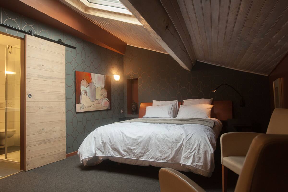 Quarto com cama, cadeira, pintura e claraboia.