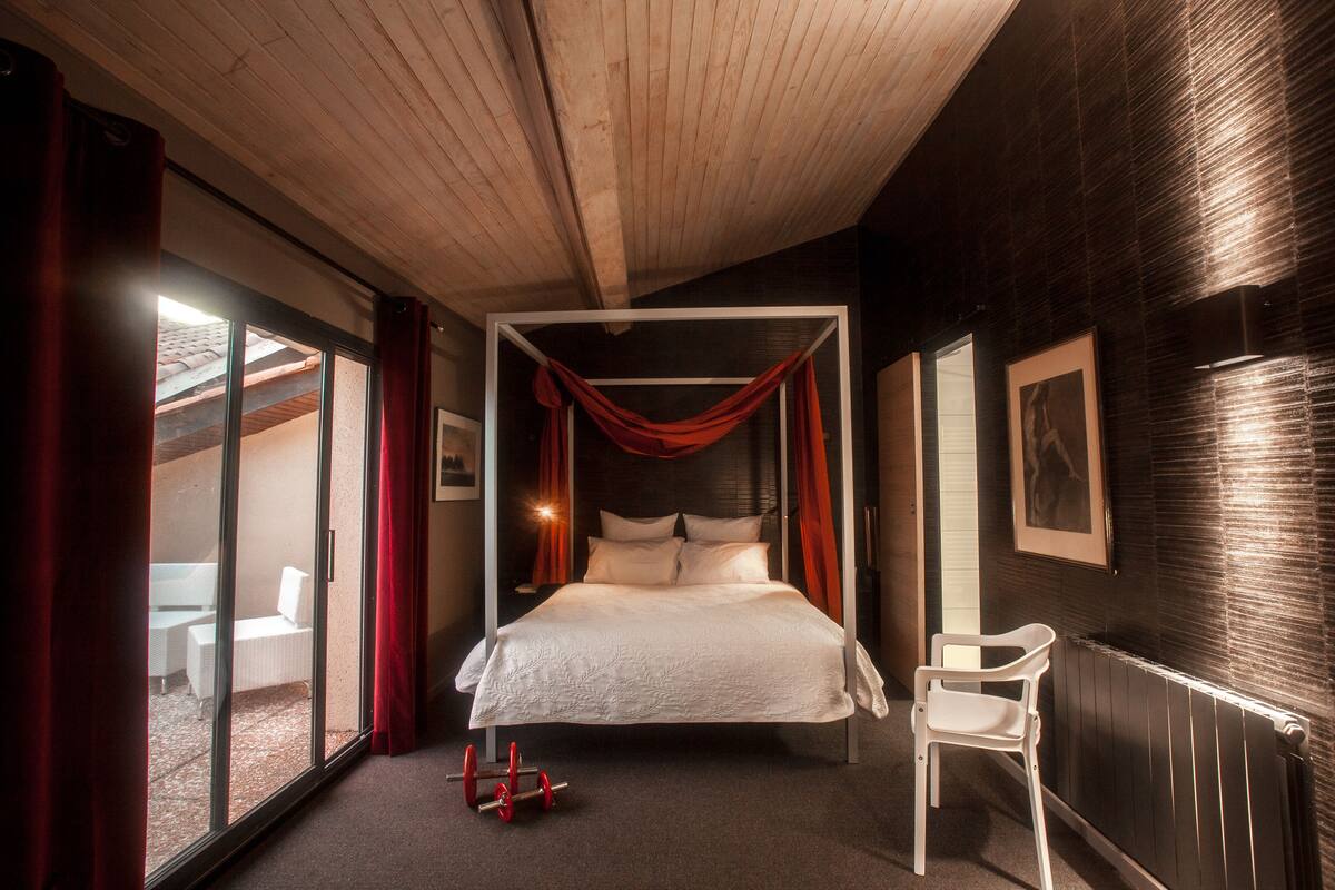 Um quarto com cama, cadeira, janela e radiador.