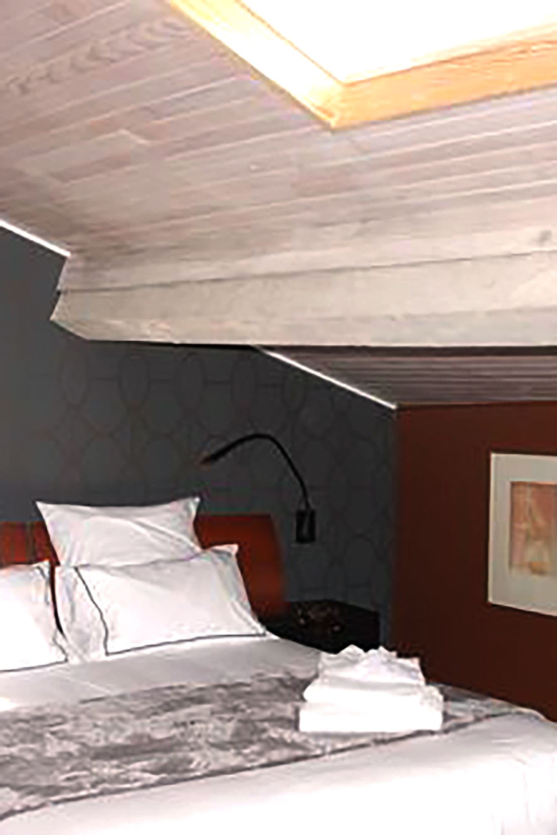 A hotel room with a bed, a nightstand, and a wall-mounted lamp.