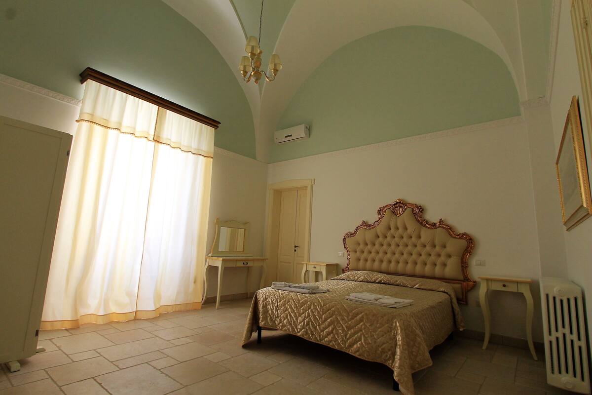 A bedroom with a large bed, a dresser, a mirror, and a radiator.