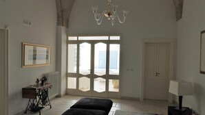 A room with a large arched ceiling, a chandelier, a sewing machine, a bed, a table with a lamp, and a view through a door. - La Casa Del Mercante (Racale)