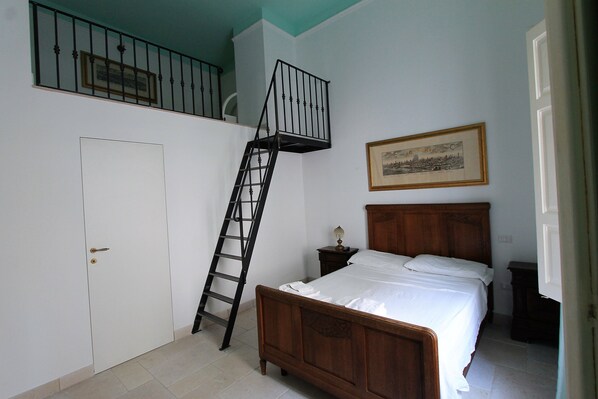 A bedroom with a wooden bed, a white door, a ladder leading to a balcony, and a framed picture on the wall.