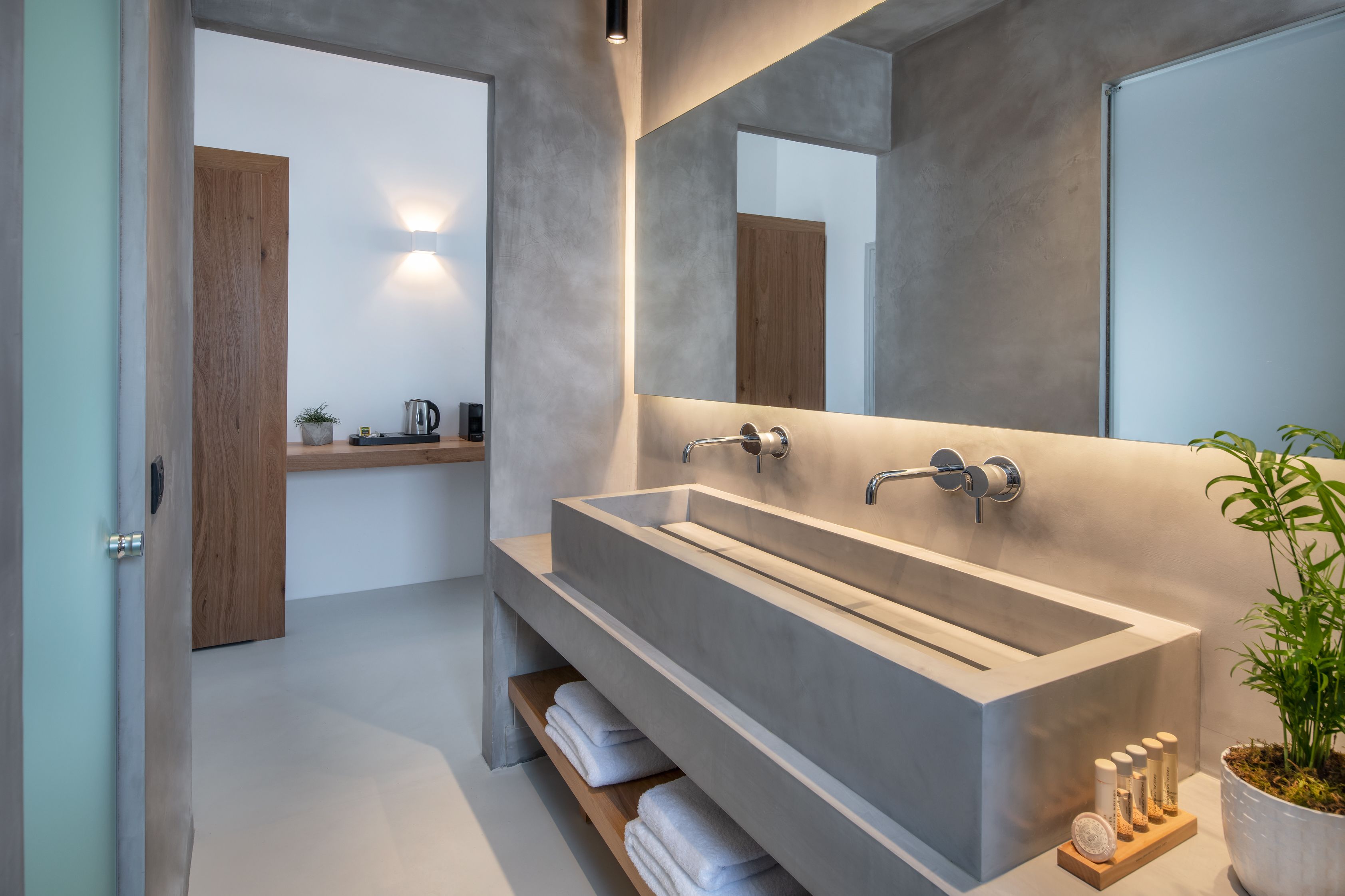 Une salle de bain moderne avec un grand lavabo rectangulaire, un miroir et une étagère où sont posées des serviettes.