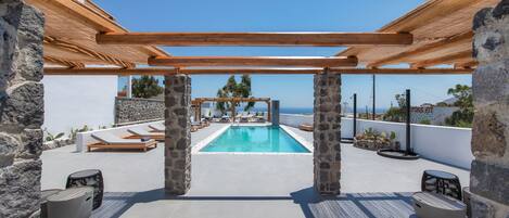 A rooftop pool area with stone pillars, wooden pergola, and lounge chairs.