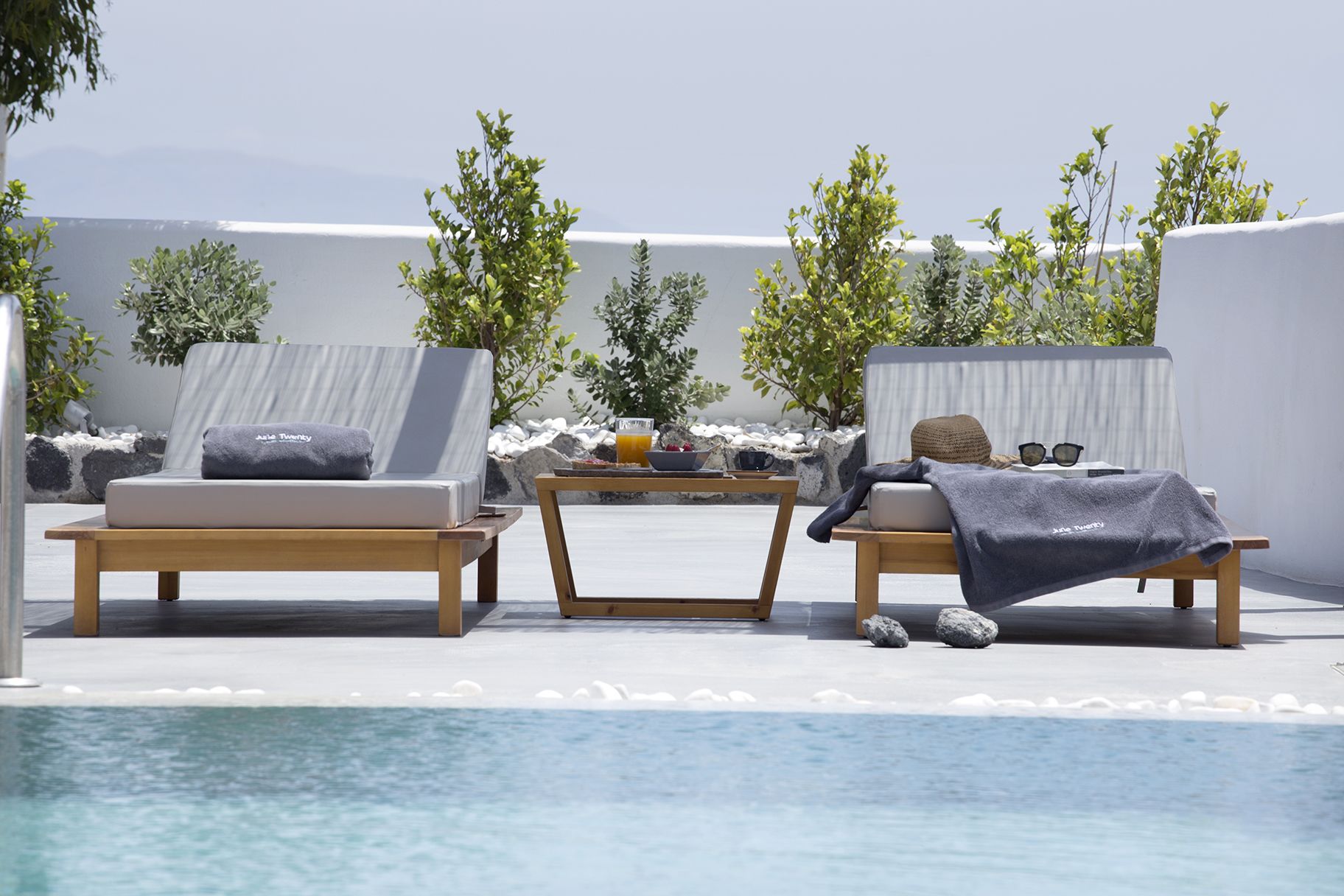 A poolside area with two lounge chairs, a table with a drink and snacks, and a view of the sea.