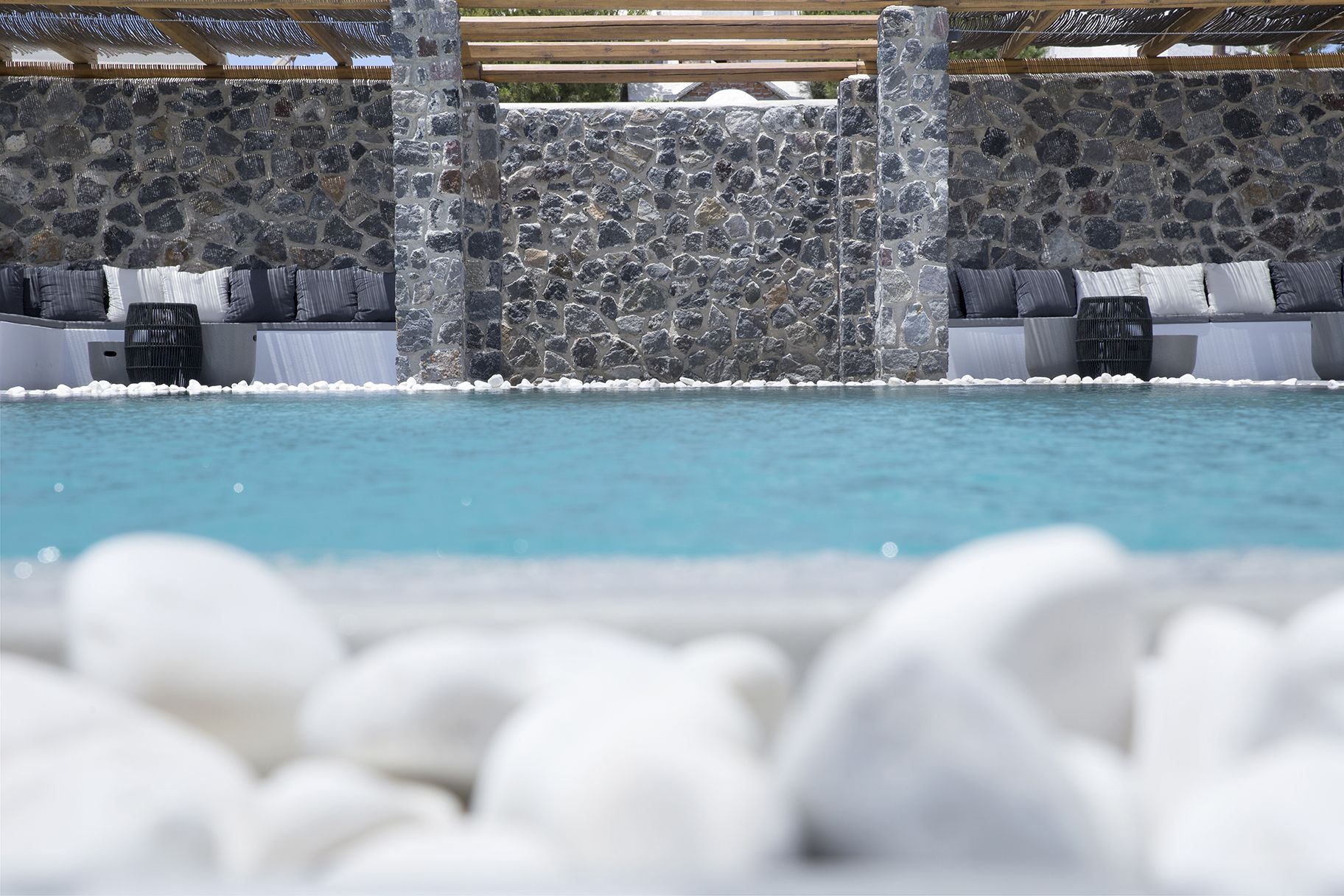 A stone wall with a pool and white pebbles in the foreground.