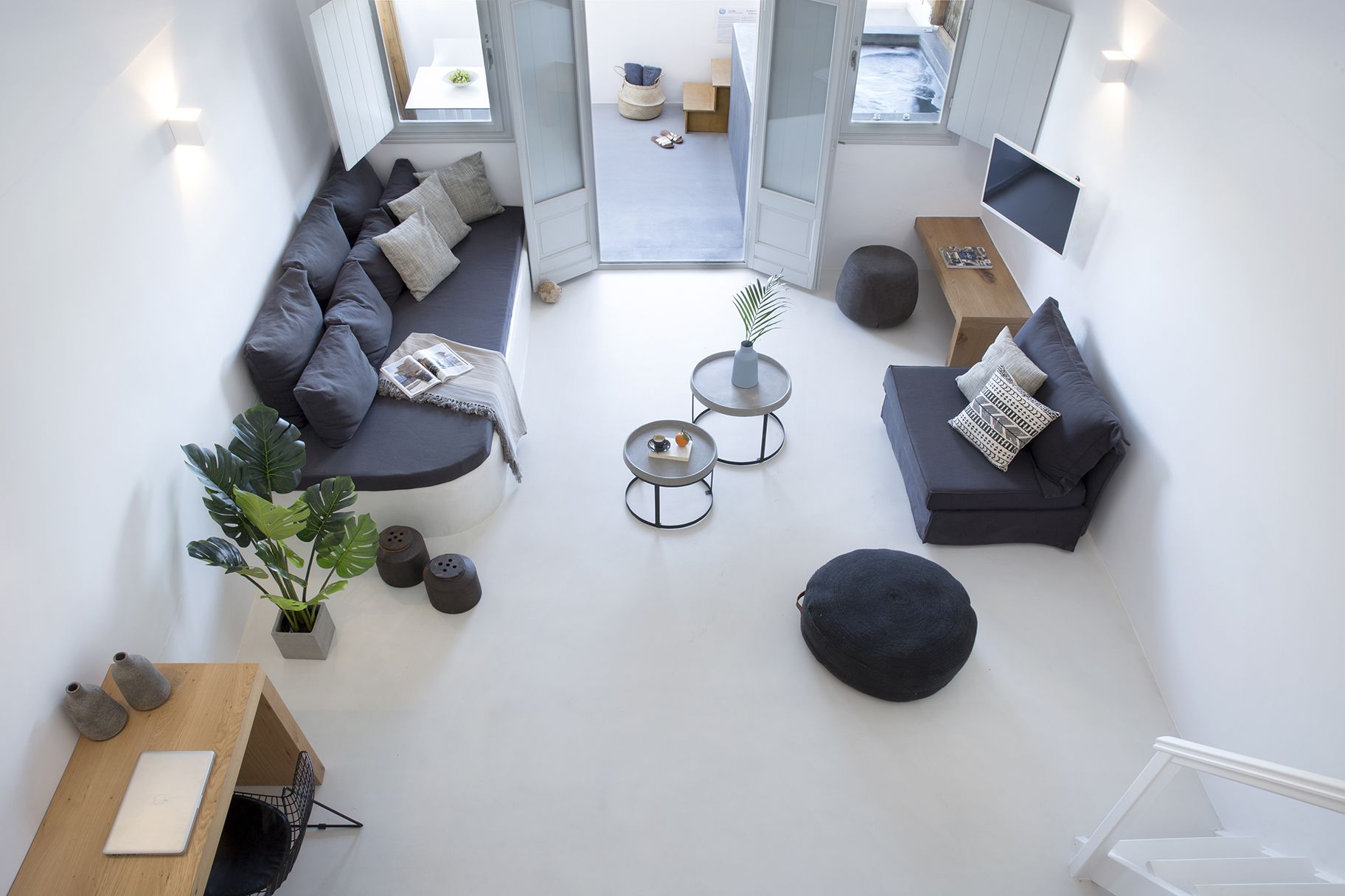 Un salon moderne avec un canapé d’angle, deux petites tables rondes, un pouf noir et une table d’appoint en bois sur laquelle se trouve un ordinateur portable.